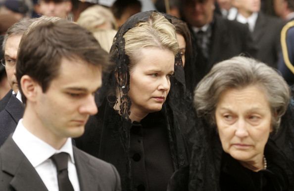 Princess Mathilde with a sad face, wearing a black scarf and black dress, and in front of her is Countess Anna Maria d'Udekem d'Acoz with a serious face and also wearing a black scarf and dress with his son Charles wearing a black suit and tie.