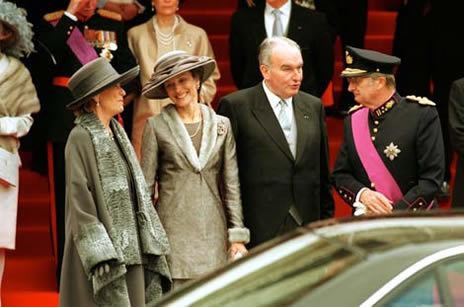 Patrick d'Udekem d'Acoz wearing a black suit while talking to a royal guard and with two ladies wearing a royal dress and hats.