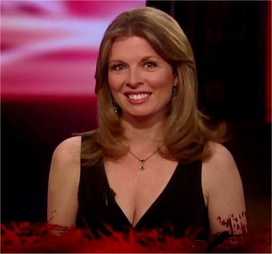 Patti Ann Browne is smiling, with a microphone on her dress, has long blonde hair, wearing earrings, a black necklace, and cleavage showing a black sleeveless dress.