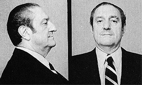 On left, Paul Castellano posing sideways and wearing a black suit as well as a black and white tie. On right, Paul Castellano smiling with the same outfit.
