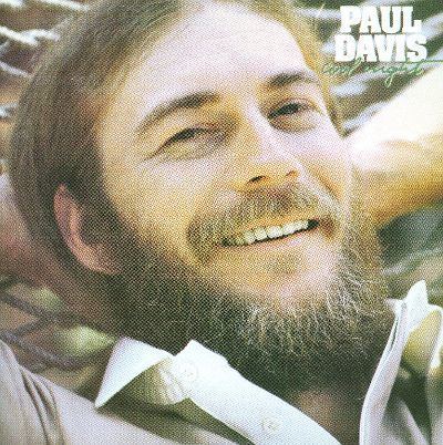Poster of Paul Davis, an American singer/songwriter, with a smiling face, with a mustache and beard.