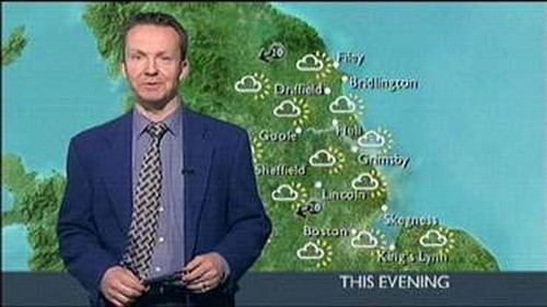 Paul Hudson presenting the weather forecast while wearing a blue coat, purple long sleeves, and black and gray necktie