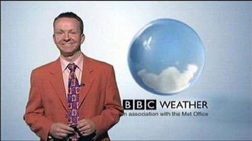 Paul Hudson smiling while wearing an orange coat, pink long sleeves, and purple necktie and behind him is the BBC Weather logo
