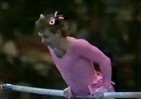 Paul Hunt wearing a pink skirted leotard and ribbon hair tie while performing a gymnastic comedy routine