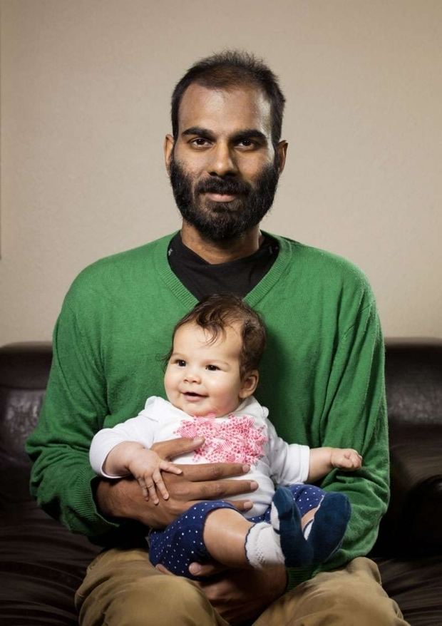 Paul Kalanithi with mustache and beard, carrying his daughter, Cady, while wearing a green sweatshirt and brown pants