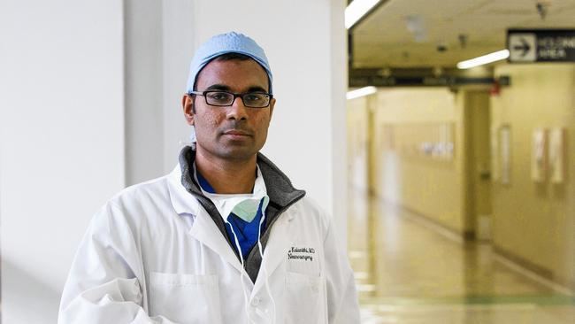 Paul Kalanithi wearing a surgical cap, lab gown, eyeglasses, facemask, gray jacket, and blue long sleeves