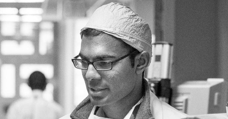 Paul Kalanithi looking at something while wearing a surgical cap, eyeglasses, and lab gown