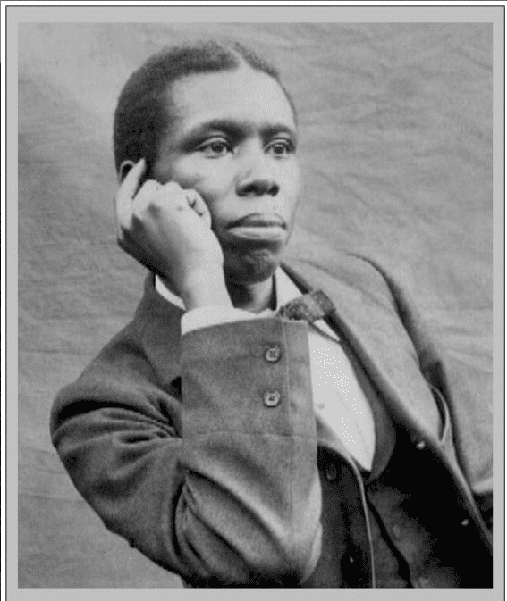 Paul Laurence Dunbar looking afar while pointing at his head with a serious face and wearing a long sleeve under a vest, bow tie, and coat