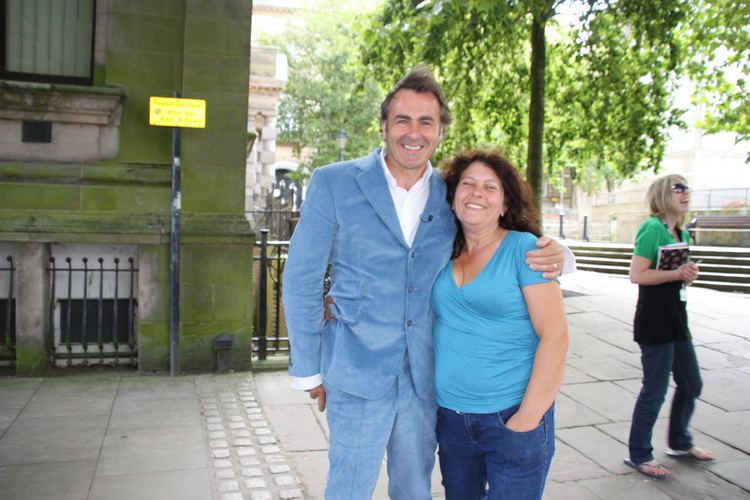 Paul Martin wearing a blue suit, a white shirt, and blue pants with a woman wearing a blue shirt and blue jeans with a girl at their back wearing sunglasses.