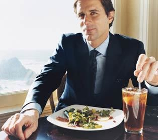 Paul Pelosi Jr. wearing a blue suit with a plate of vegetables and a glass of drink on the table.