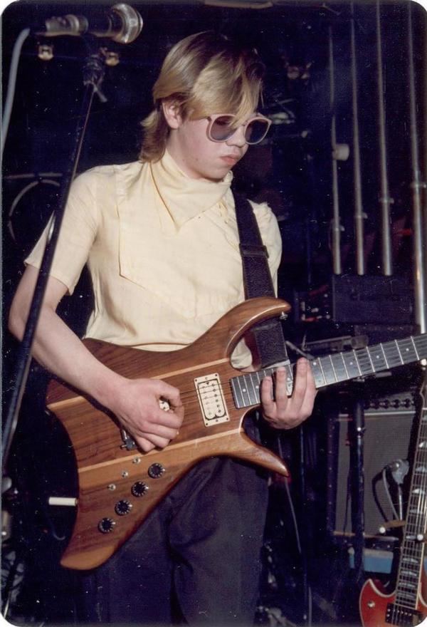 Paul Reynolds playing guitar while wearing a yellow shirt, black pants, and pink shades
