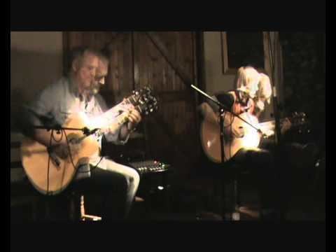 Paul Reynolds playing guitar with the man beside him while sitting on the chair