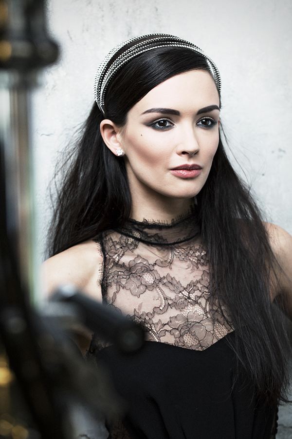 Paulina Andreeva looking afar while wearing a black lace sleeveless blouse, earrings, and headband