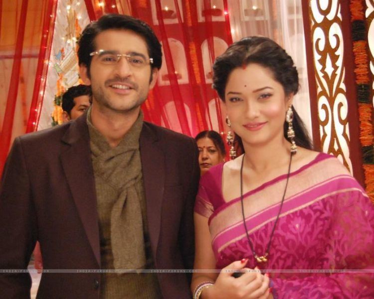 Hiten Tejwani smiling while wearing a maroon coat and brown inner shirt while Ankita Lokhande wearing a pink dress