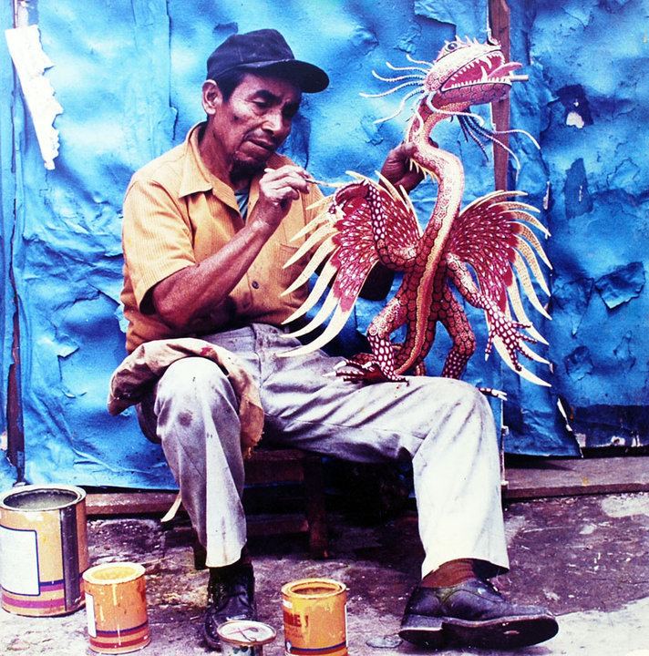 Pedro Linares sitting and making an Alebrijes Dragon while wearing a yellow sleeve