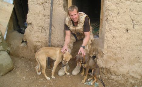 Pen Farthing smiling and wearing a royal marine uniform while two brown dogs are beside him