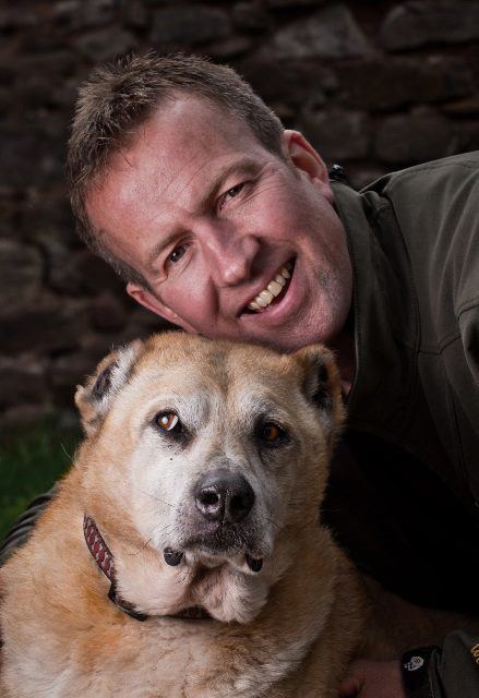 Pen Farthing smiling with his dog while he is wearing a gray shirt
