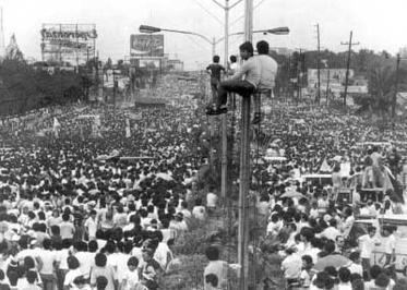 The EDSA road full of people protesting against Marcos reign with some even climbing on the light posts