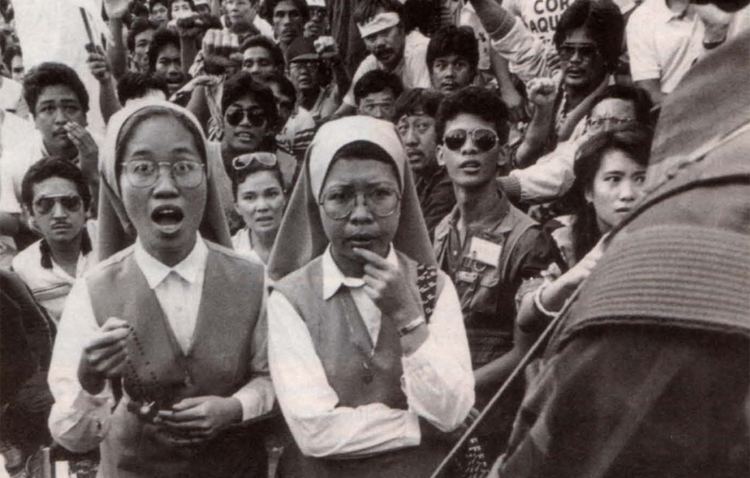 Two nuns saying the rosary during  the second day of the People Power Revolution with an army in front of them and with the crowd protesting from behind