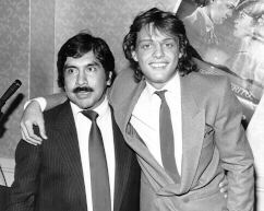 Pepe Barreto with a mustache, wearing a suit and a tie with a man with long hair, also wearing a suit and a tie.