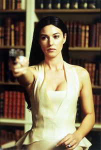 Monica Bellucci as Persephone holding a gun while wearing a cream sleeveless dress