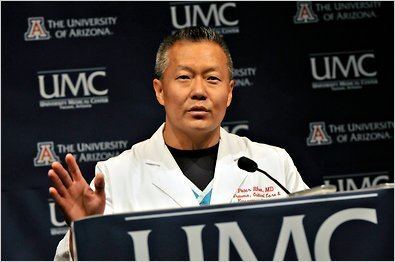 Peter M. Rhee talking on stage and wearing a white doctors attire with a black shirt underneath.