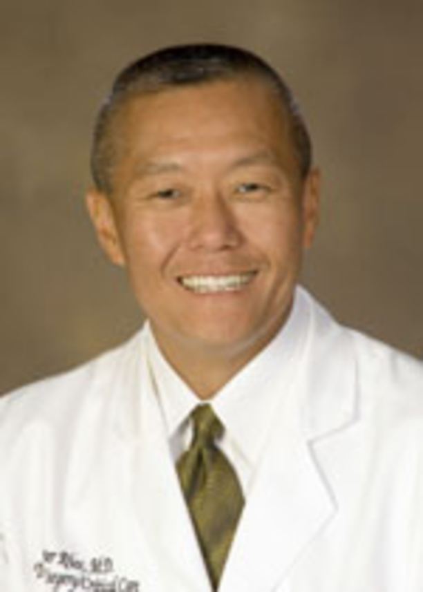 Peter M. Rhee smiling and wearing a white shirt and coat along with a brown tie.