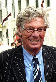 Peter van Straaten smiling while wearing a black striped coat, blue long sleeves, and striped necktie