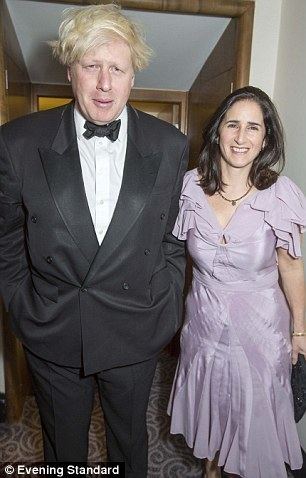 from left, Boris Johnson smiling, standing, both hands in his pocket, has blonde hair, wearing a white polo with black bowtie and a black coat with black pants, at the right, Petronella Wyatt is smiling, standing, left hand down holding a black bag, has long black hair wearing a black necklace, silver bracelet and a purple wavy dress.