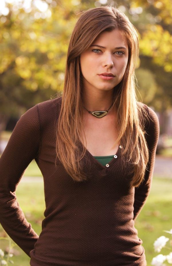 Peyton List with a fierce look and golden brown hair while wearing a necklace and green inner top underneath the brown long sleeve blouse