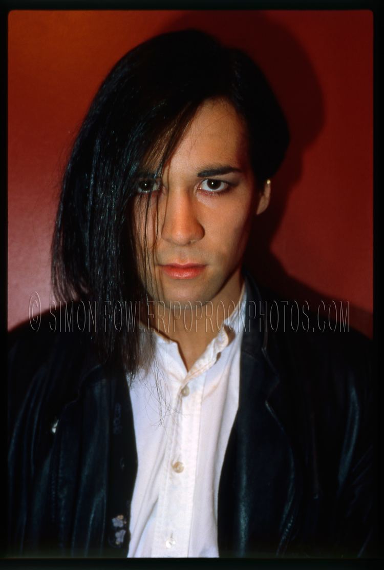 Philip Oakey with his long bangs and a fierce look wearing a white shirt and a black coat