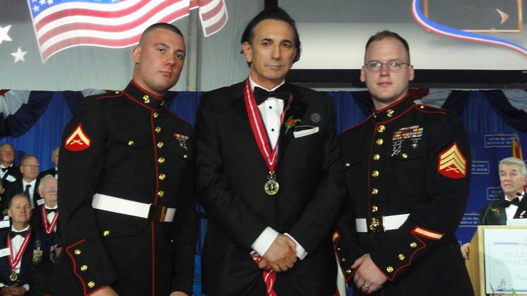 Philip Zepter posing with two men beside him while wearing a black coat, white long sleeves, bow tie, and medallion