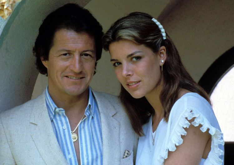 Philippe Junot smiling and wearing a gray coat and striped long sleeves while Princess Caroline of Monaco wearing a white dress