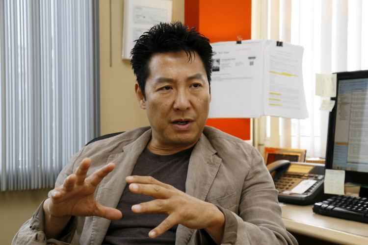 Phillip Rhee talking to someone while wearing a brown jacket and black shirt