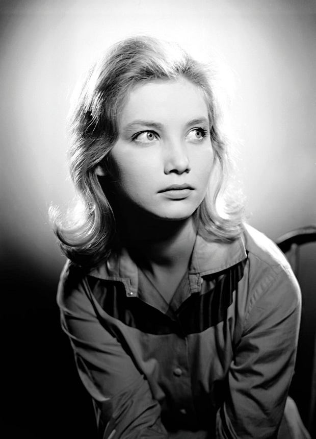 Pola Raksa with a serious face, short blonde hair, and wearing a polo shirt while sitting on a chair.