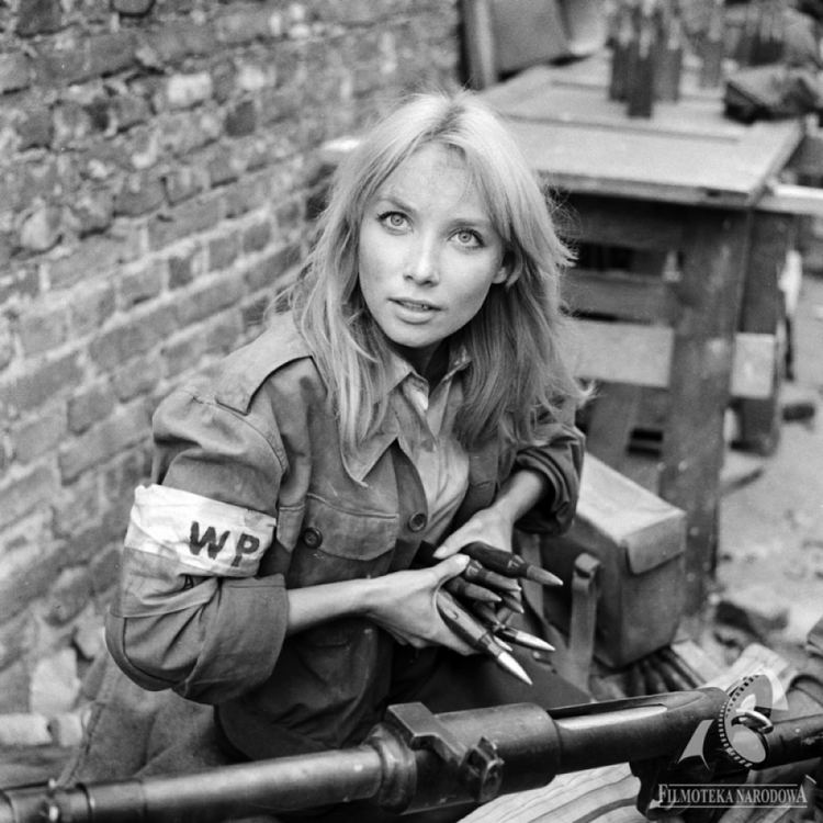 Pola Raksa with long blonde hair, wearing a dirty jacket while holding bullets.