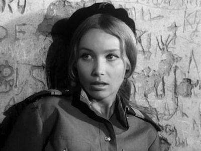 Pola Raksa with a serious face, wearing a black hat and a uniform while leaning on the wall.