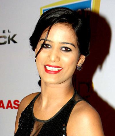 Poonam Pandey  smiling with her tie black hair with a few strands covering her eyes, wearing an earring and a see-through black sleeveless