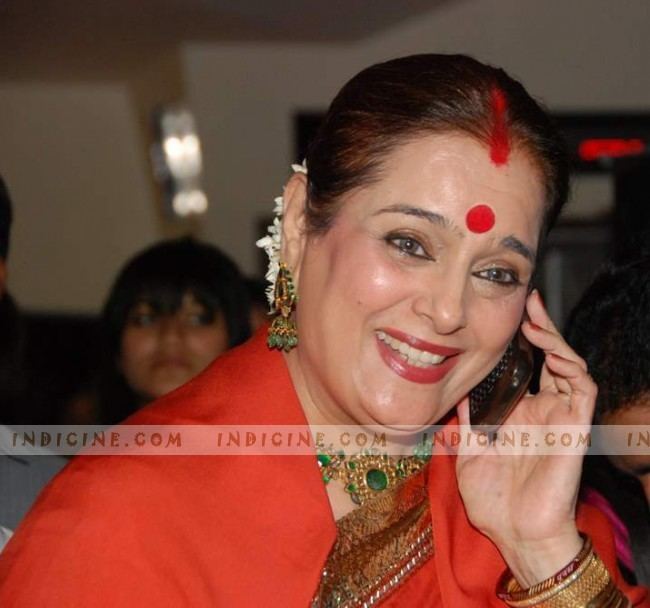 Poonam Sinha smiling and holding her phone while wearing red dress, earrings and necklace