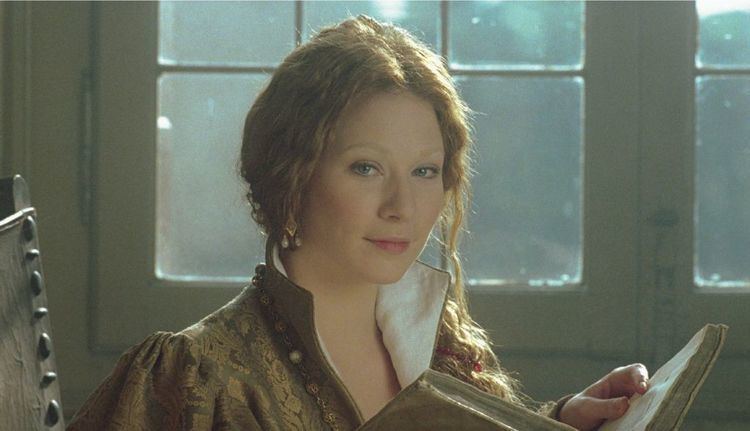 Lynn Collins smiling and holding a book as she plays the role of Portia in "The Merchant of Venice"