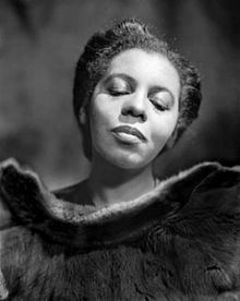 Portia White in 1946, with a tight-lipped smile, her eyes are closed, and tied-up hair while wearing a blouse with fur