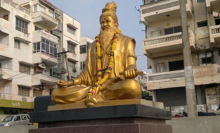 A gold plated statue of Pothuluru Veerabrahmendra with a garland of flowers.