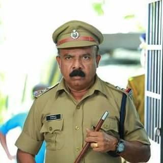 Pradeep Kottayam looking angry and holding a baton as he plays the role of a head constable in the in the 2015 film "Aadu Oru Bheegara Jeevi aanu" and wearing an officer uniform