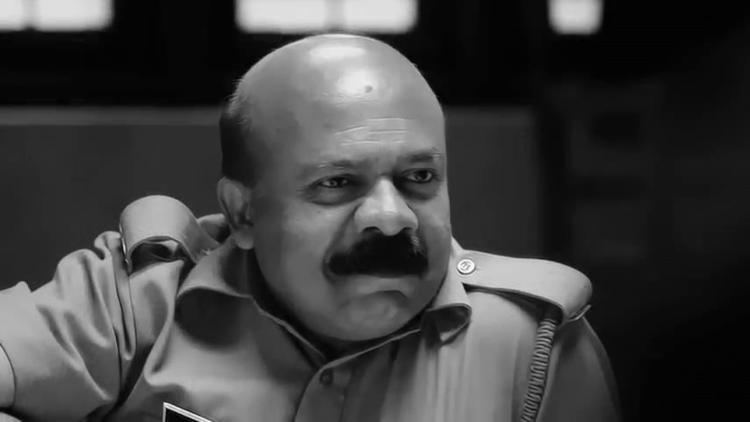 Pradeep Kottayam smiling with a bald head and a mustache playing the role of a head constable in the 2015 film "Aadu Oru Bheegara Jeevi aanu" and wearing an officer uniform.