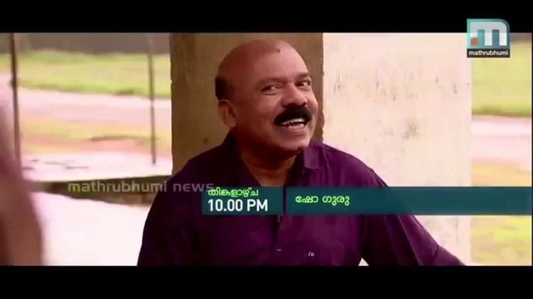 Pradeep Kottayam smiling as flashed in a news channel with a bald head and mustache while wearing a violet long-sleeve shirt