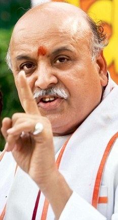 Pravin Togadia speaking while pointing his finger and wearing a white shirt and white and orange sash