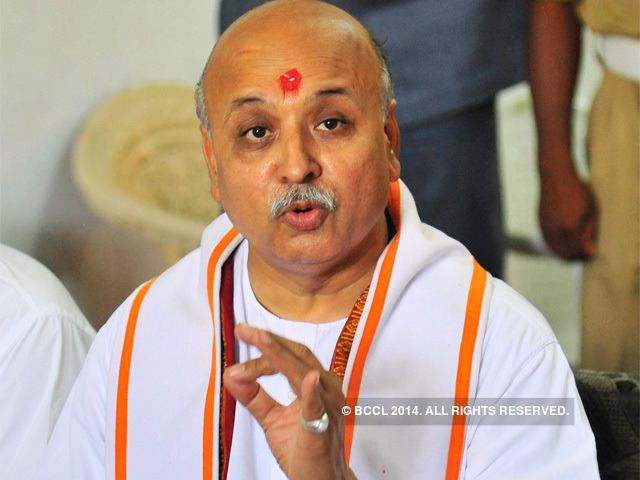 Pravin Togadia speaking with hand gesture while wearing a white shirt and white and orange sash