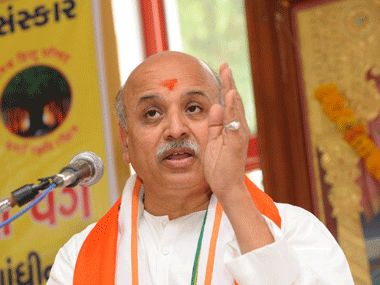 Pravin Togadia speaking with hand gesture while wearing a white shirt and white and orange sash