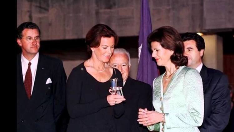 Anni-Frid Lyngstad smiling and wearing a black dress while Drottning Silvia wearing a green dress and three men behind them