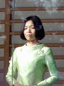 Princess Akiko of Mikasa with a serious face, with short black hair, wearing a pearl necklace and a mint green long sleeve dress.